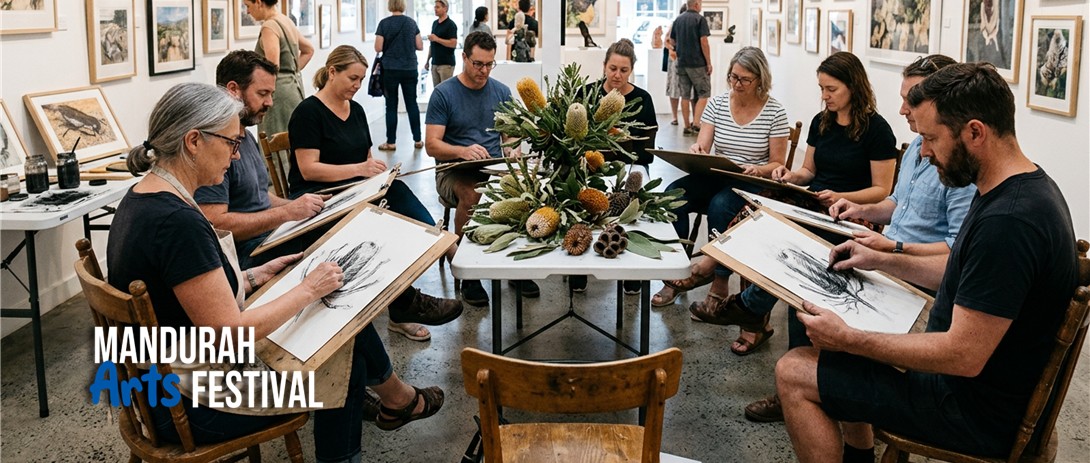 A group of people sit around a table which is covered in banksias, sketching the flowers on large paper with charcoal
